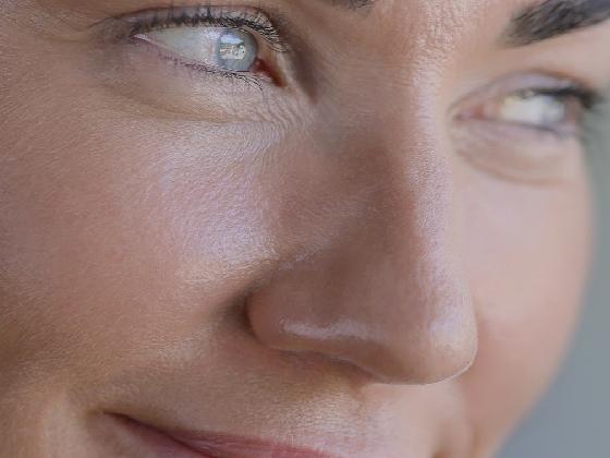 Close-up of a person's face, showing smooth skin, a slight smile, and bright eyes looking to the side.