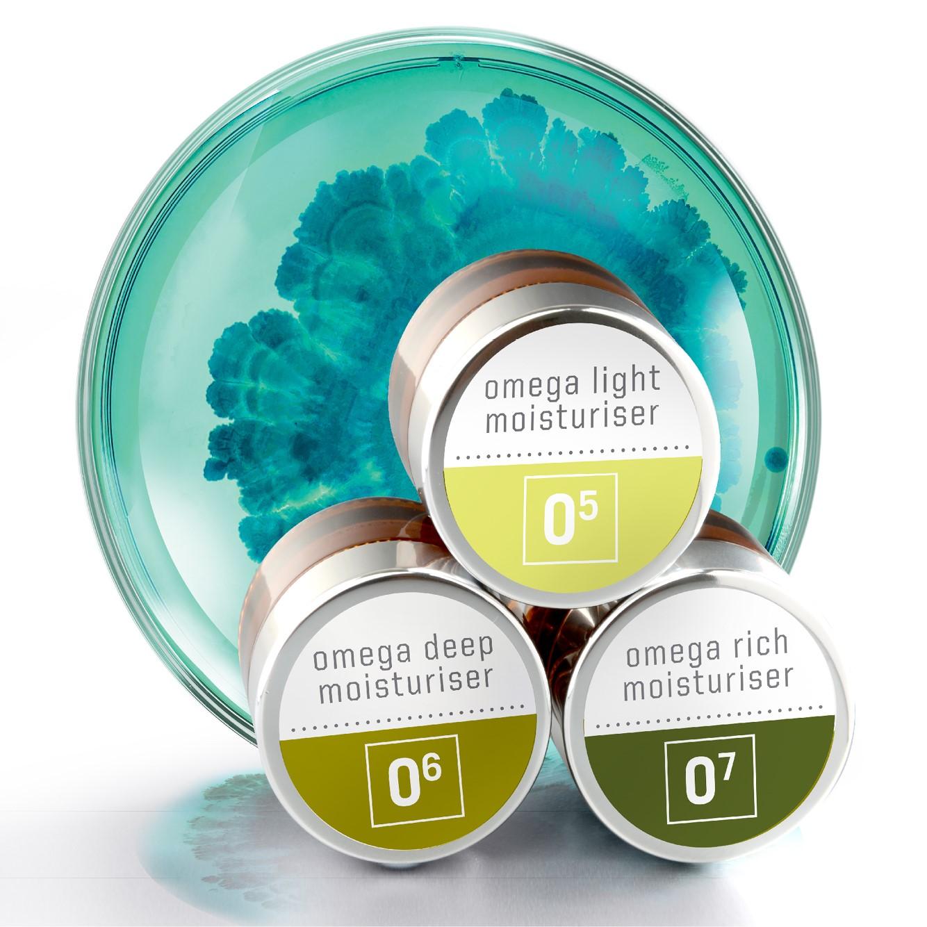 Three skincare jars labeled "omega light moisturiser," "omega deep moisturiser," and "omega rich moisturiser" are stacked in front of a round dish with a teal, abstract swirling pattern.