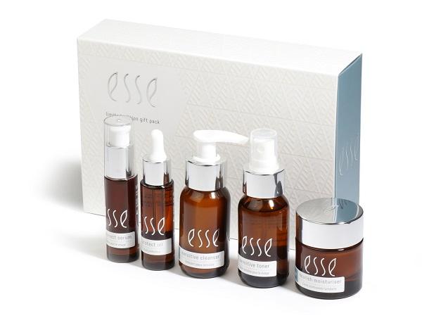 Five amber glass skincare bottles and jars labeled "Esse" are displayed in front of a white textured gift box with the same branding. The containers vary in size and have pumps, droppers, or screw-top lids.