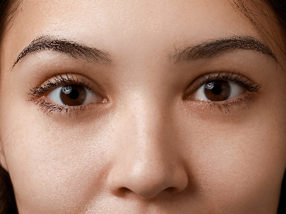 A close-up photo of a person's face, focusing on their eyes, brows, and the bridge of their nose. The skin appears smooth and natural, with minimal makeup visible.