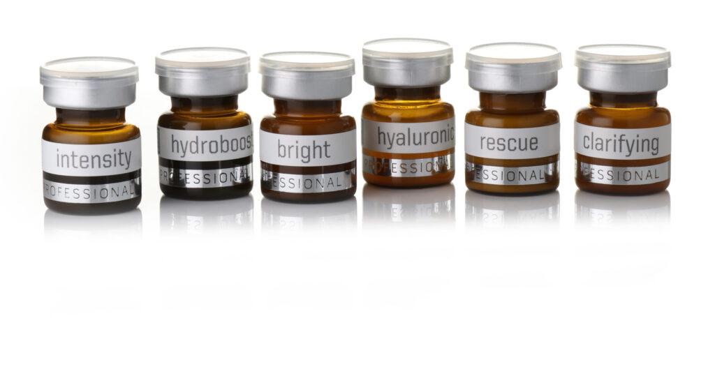 Six small brown bottles with silver caps, each labeled with different words: intensity, hydroboost, bright, hyaluronic, rescue, and clarifying, arranged in a row on a white background.